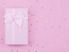 Pink gift box wrapped in a pink ribbon on a pink, starry background. 