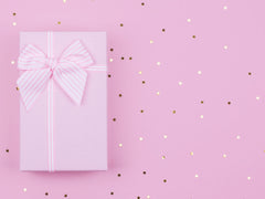 Pink gift box wrapped in a pink ribbon on a pink, starry background.